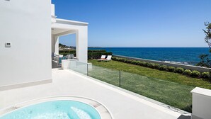 A modern outdoor pool area with a view of the sea, a lounge with chairs, and a glass balustrade.