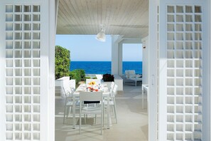 An open-air dining area with a view of the sea, white furniture, and a ceiling fan. - Mariol - 4 People, Jacuzzi, on the Sea, Garden, Wifi, A/C (Fontane Bianche)