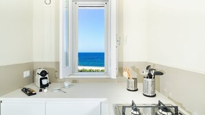 A compact kitchen with a view of the sea, a coffee maker, utensils, and a gas stove.