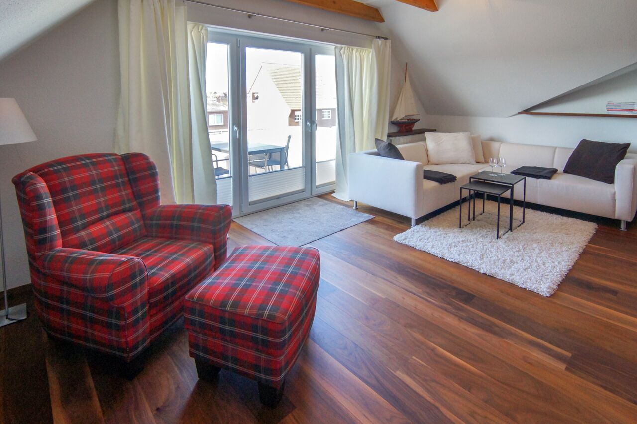 A living room with a red plaid sofa, a matching ottoman, a white sofa, and a small table with a glass.