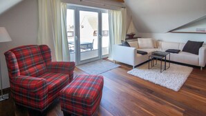 A living room with a red plaid sofa, a matching ottoman, a white sofa, and a small table with a glass. - Vacation apartment Norddeich Loft (Norddeich)
