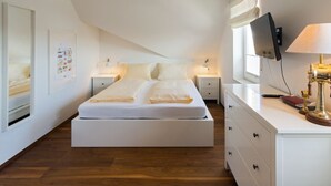 A modern bedroom with a large bed, bedside tables, a TV, and a lamp. - Vacation apartment Norddeich Loft (Norddeich)