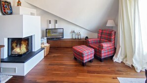 A cozy living room with a fireplace, plaid armchairs, a television, and a lamp. - Vacation apartment Norddeich Loft (Norddeich)
