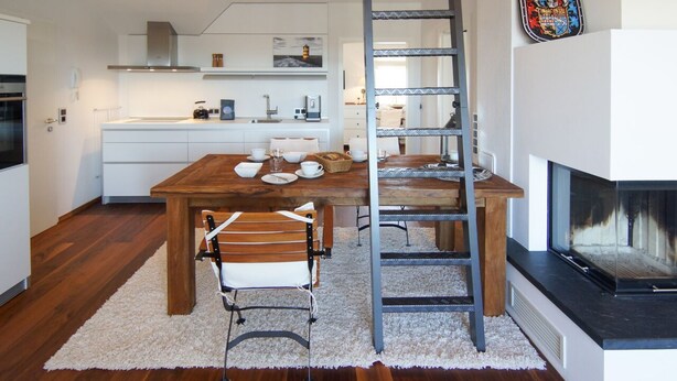 A modern kitchen with a wooden dining table, white cabinets, and a fireplace. - Vacation apartment Norddeich Loft (Norddeich)