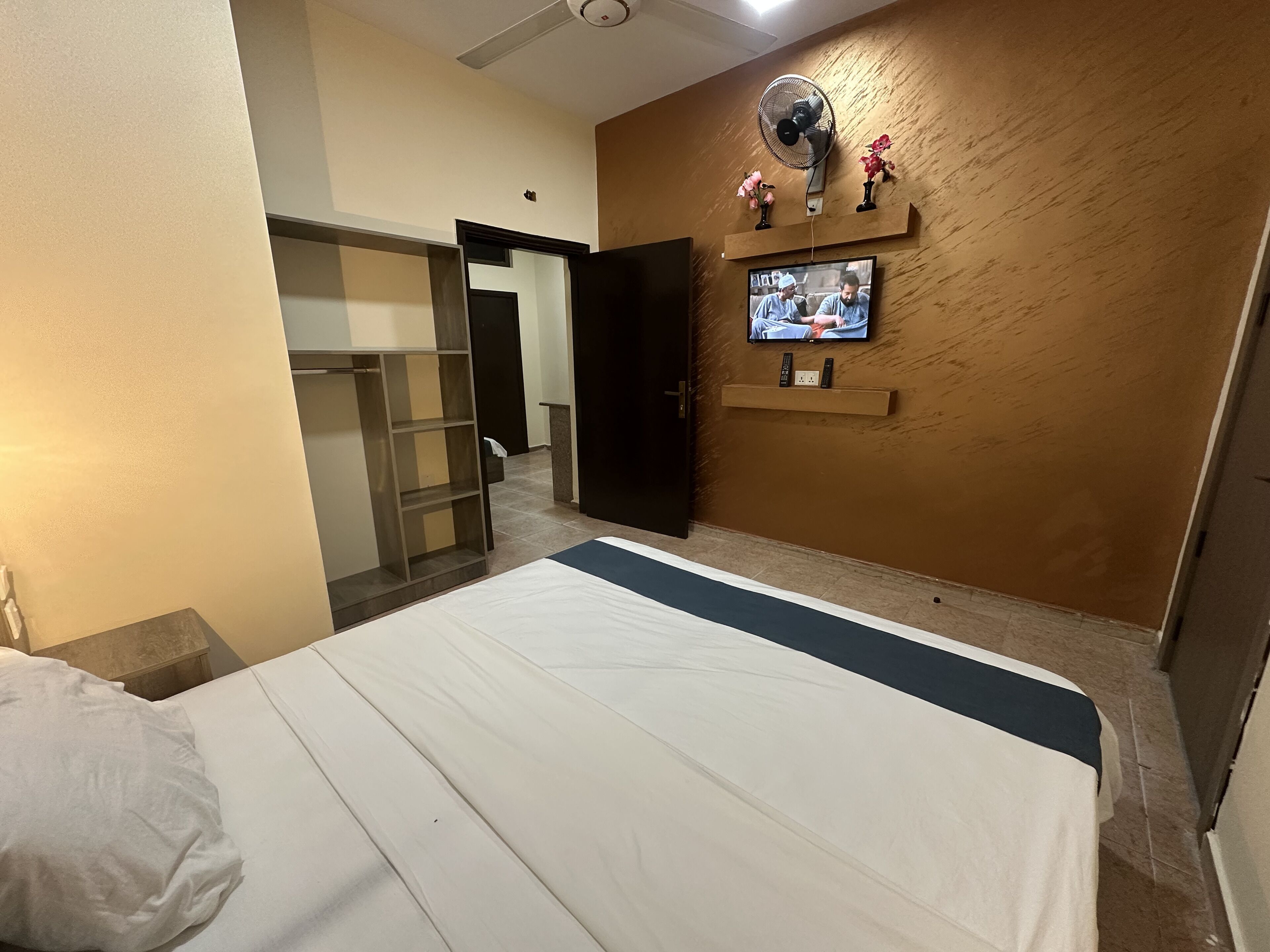 Una camera d'albergo con un letto, un armadio, una TV a parete e una ventola a soffitto.