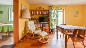 Un accogliente soggiorno con un tavolo da pranzo in legno, una poltrona a dondolo, una libreria e una pianta in vaso.