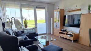 Ein modernes Wohnzimmer mit einer Sofagarnitur, einem Glastisch, einem Fernseher und einer Holzkommode.