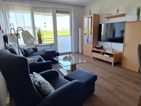 A modern living room with a sofa set, a glass coffee table, a TV, and a wooden cabinet. - Close to the beach... directly behind the dike! (Dahme)