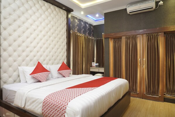 A hotel room with a large bed, a tufted headboard, a red and white patterned bedspread, and a wooden wardrobe with curtains.
