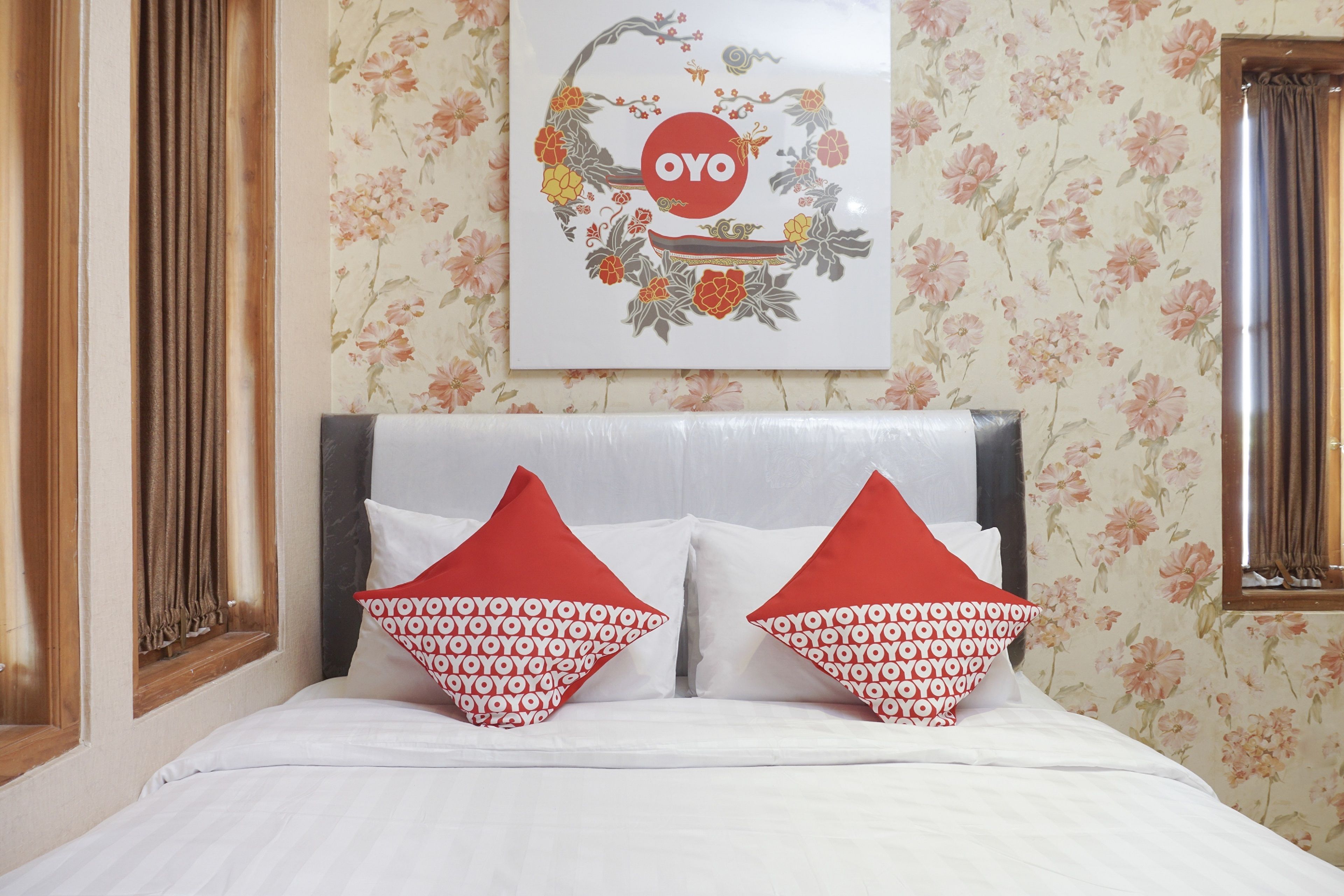 A neatly made bed with white bedding and two red pillows with a repeating pattern.