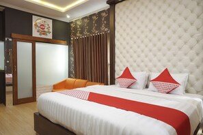 A hotel room with a large bed, a wooden chair, a wardrobe, and a door leading to another room.