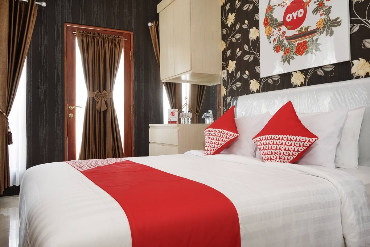 A hotel room with a large bed, a wooden wardrobe, a white bedside table, and a floral wallpaper.