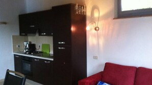 A compact living space with a kitchenette, a red sofa, and a window. - Eco house with pool and fantastic views (Scansano)
