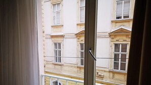 Une vue à travers une fenêtre à cadre blanc, dévoilant la façade d’un immeuble avec de nombreuses fenêtres et une balustrade de balcon.