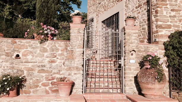A stone building with a gated entrance, terracotta pots with flowers, and a staircase leading up to the door. - UNIQUE LARGE TERRACE WITH VIEWS TO CHAINTI VALLEY AND DRINK (Ruffoli)
