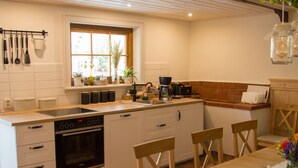 Una cocina compacta con armarios blancos, horno integrado, cafetera y ventana con plantas.