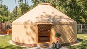 Una yurta con puerta de madera, un pequeño porche y una maceta a su lado.