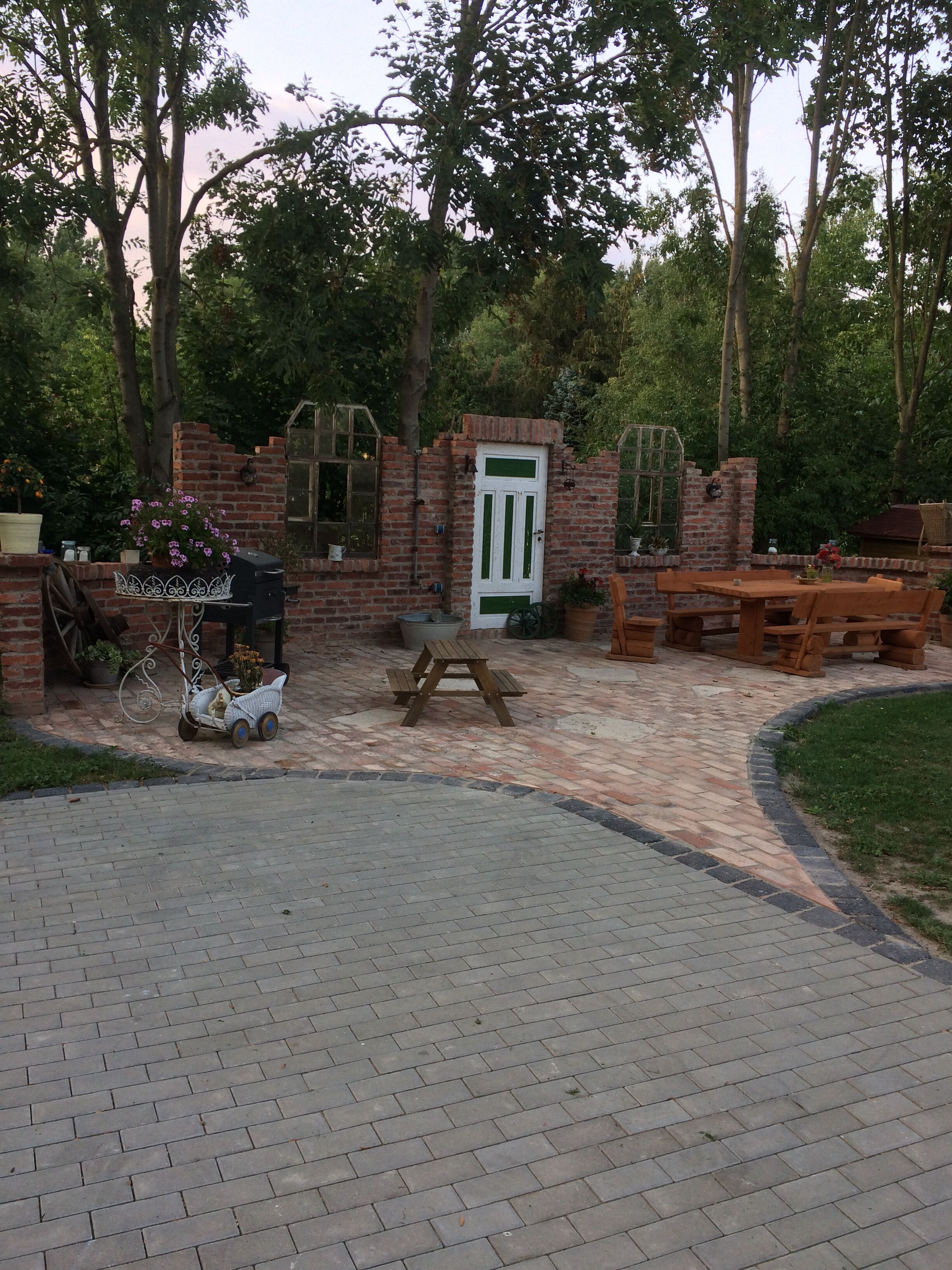 Une terrasse en briques avec une porte blanche, des bancs en bois et une petite table.