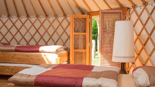 Interior acogedor de una yurta con dos camas, una puerta de madera y una lámpara.