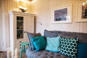 A cozy room with a cushioned sofa, a wooden cabinet with glass doors, and a framed picture on the wall.
