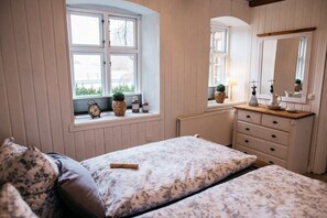A bedroom with two beds, a dresser, a mirror, and a window with a view of trees.
