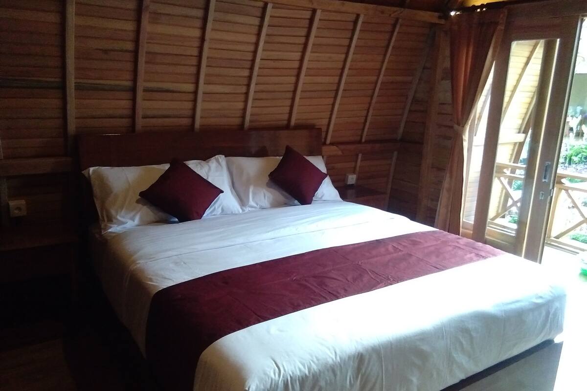 A wooden-framed room with a bed, white bedding, and two red pillows.