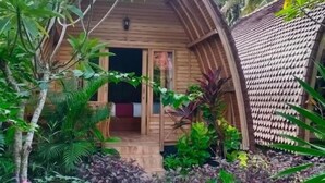 A wooden cabin with a sloped roof, surrounded by lush greenery and tropical plants. - Visual Inn (Penida Island)
