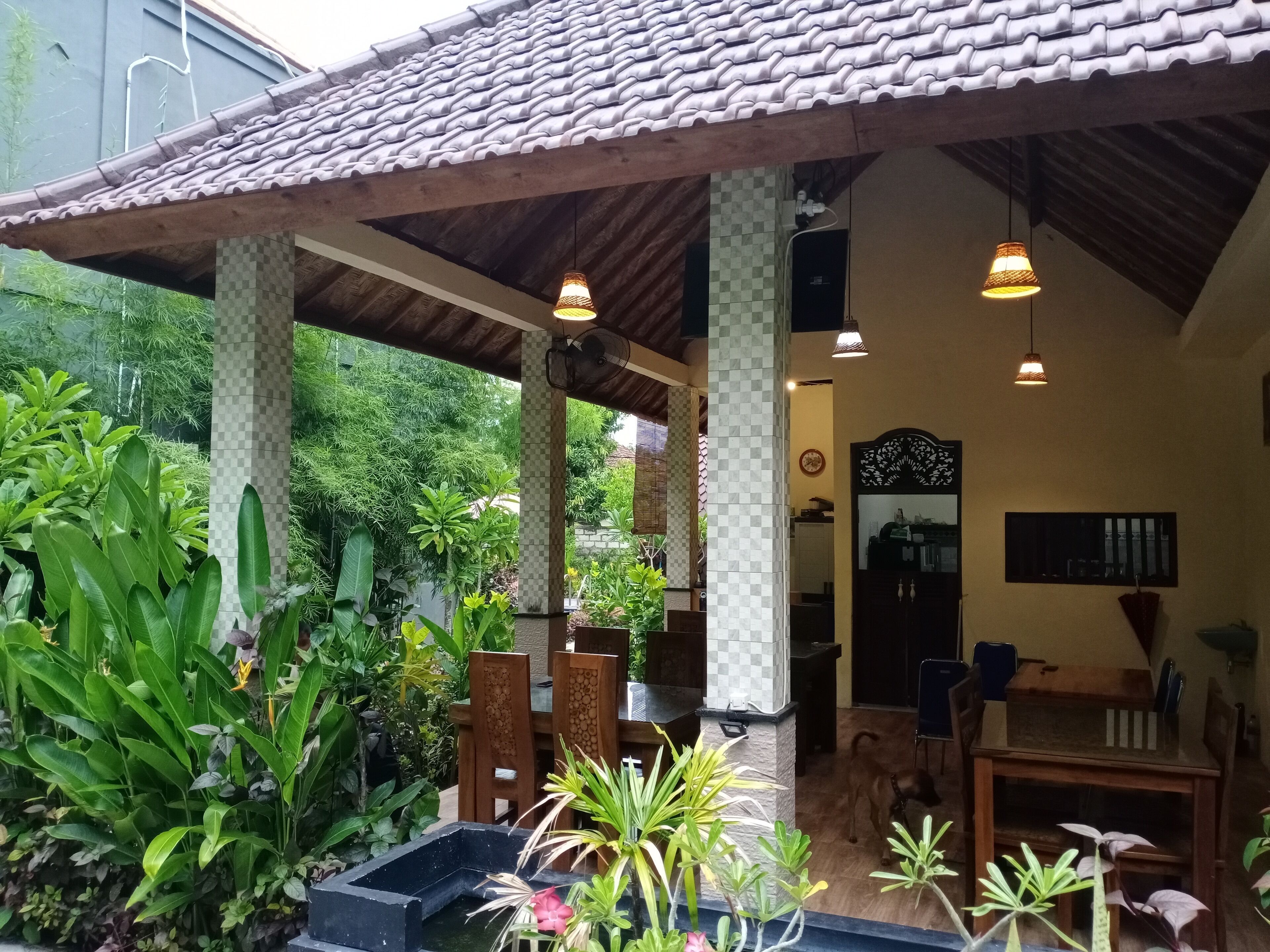 A covered outdoor area with a tiled roof, wooden furniture, and various plants.