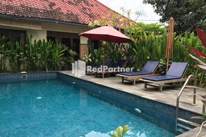 A swimming pool with lounge chairs and an umbrella, surrounded by lush greenery. - Visual Inn (Penida Island)