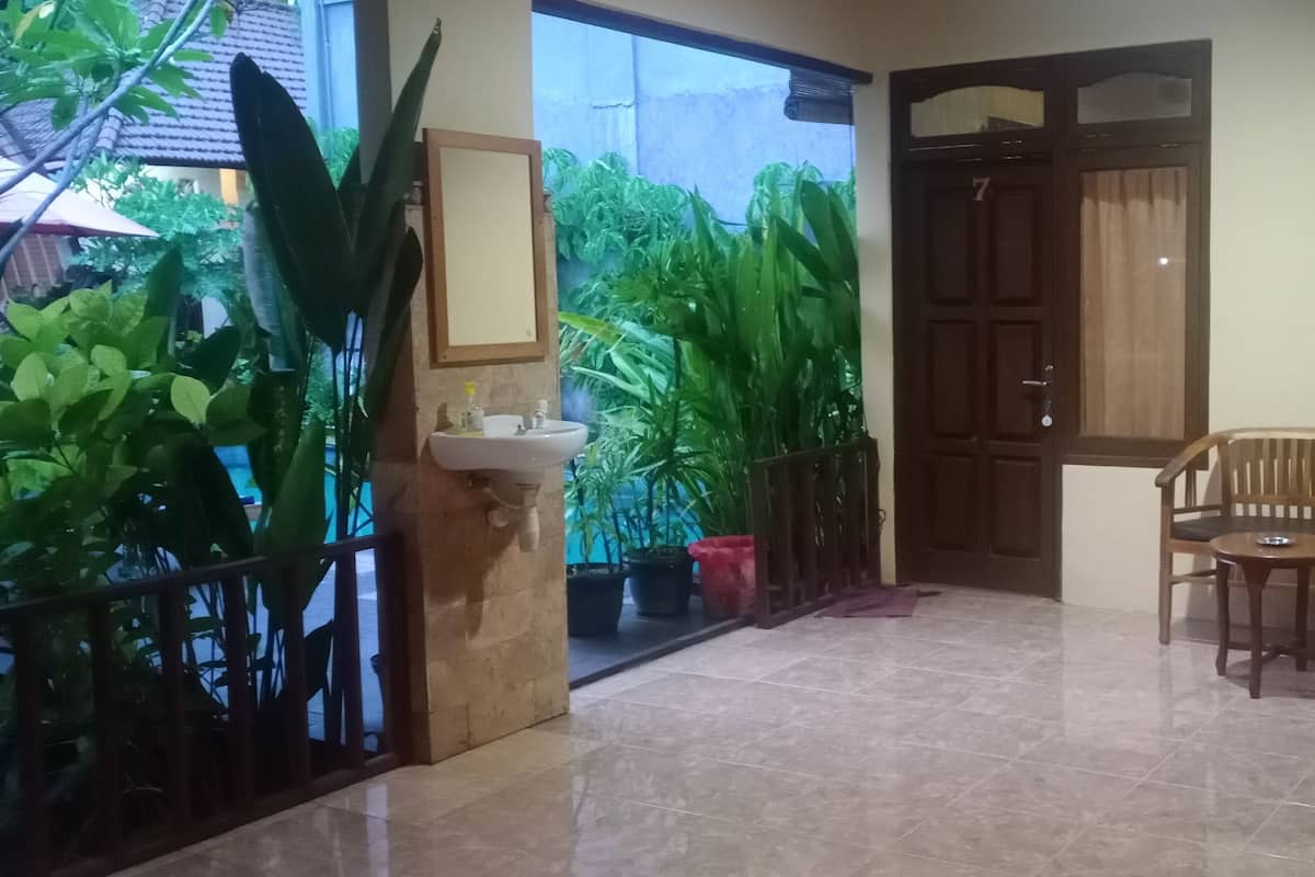 A balcony with a wooden bench, a potted plant, and a door leading to a garden area.