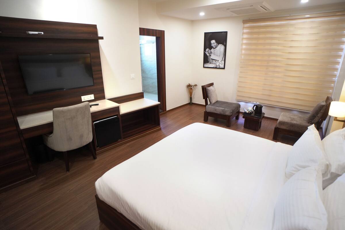 Una habitación de hotel con una cama grande, un escritorio con silla, un televisor, una ventana con persianas y un cartel en la pared.