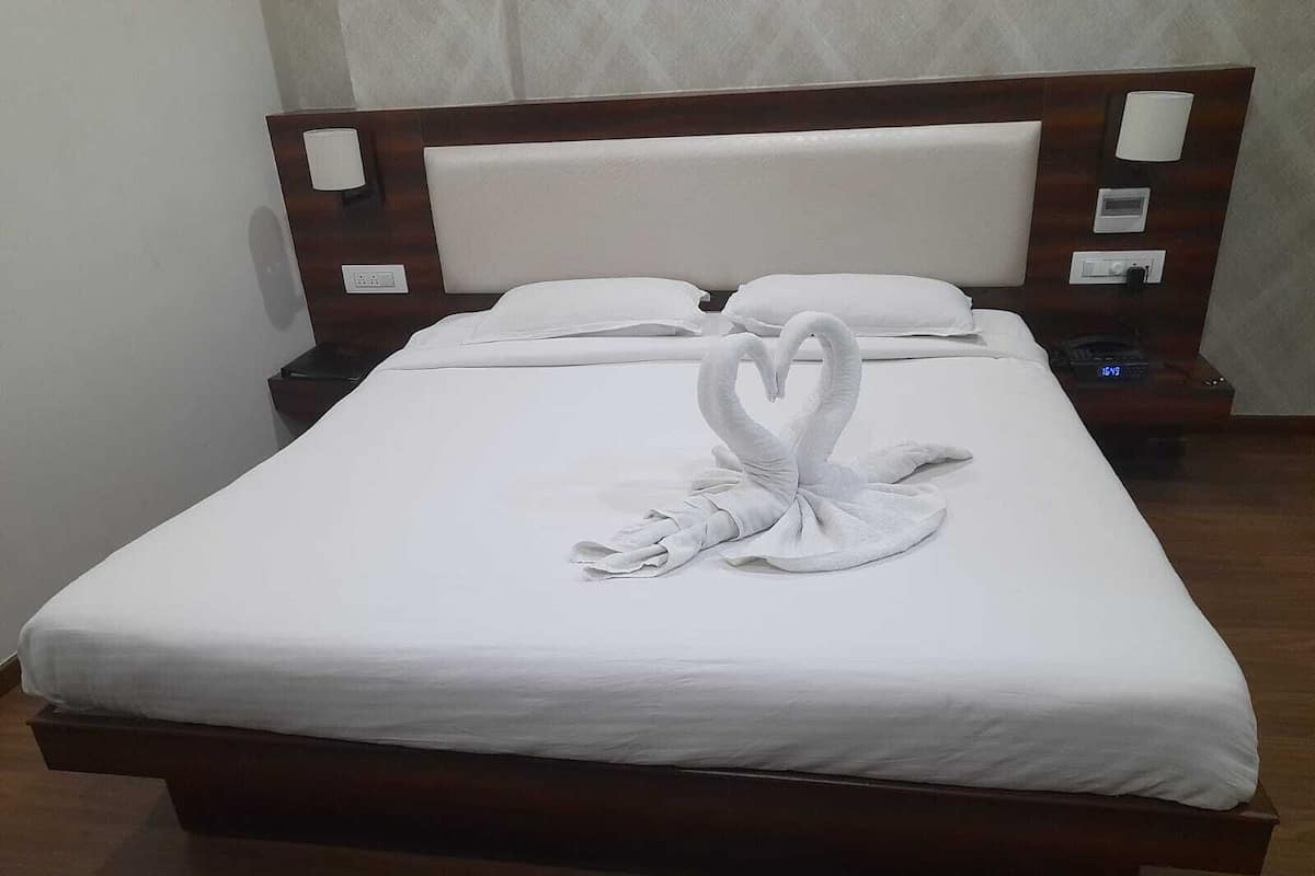 Una cama bien hecha con una escultura de cisne de toallas, un cabecero de madera y controles junto a la cama.