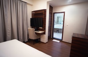 Habitación de hotel con cama, escritorio, silla, televisor y puerta corredera al baño.