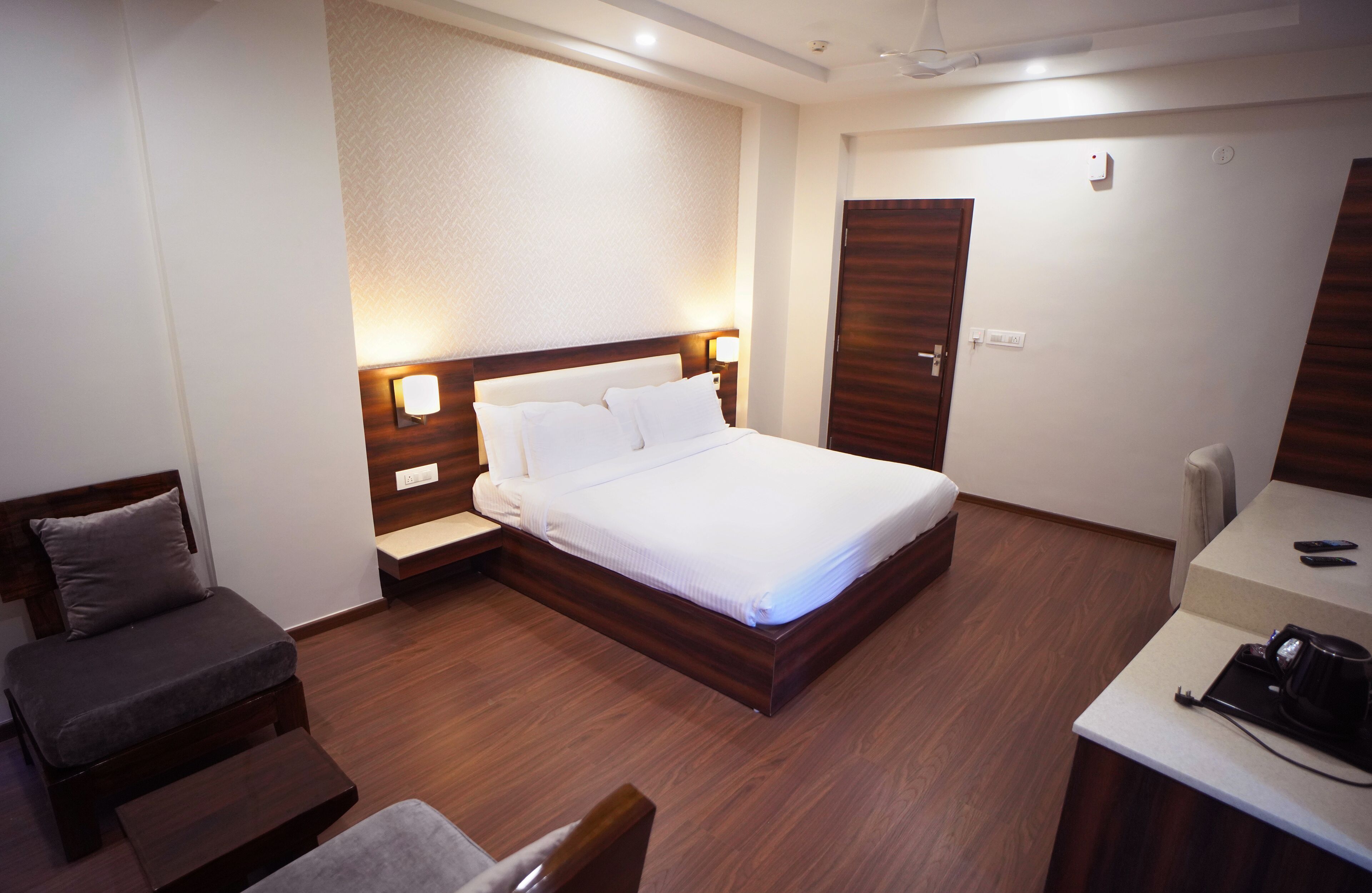 A hotel room with a bed, bedside tables, a desk with a chair, and a wardrobe.