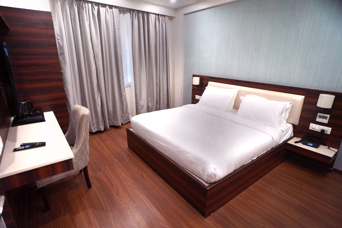 Una habitación de hotel con una cama de madera, un escritorio con una silla, un televisor y una mesita de noche con una lámpara.