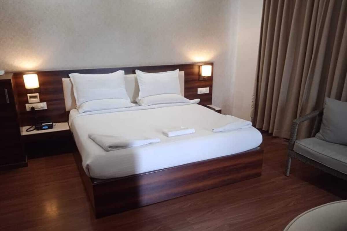Una cama bien hecha con sábanas blancas, un cabecero de madera y dos mesitas de noche con lámparas.