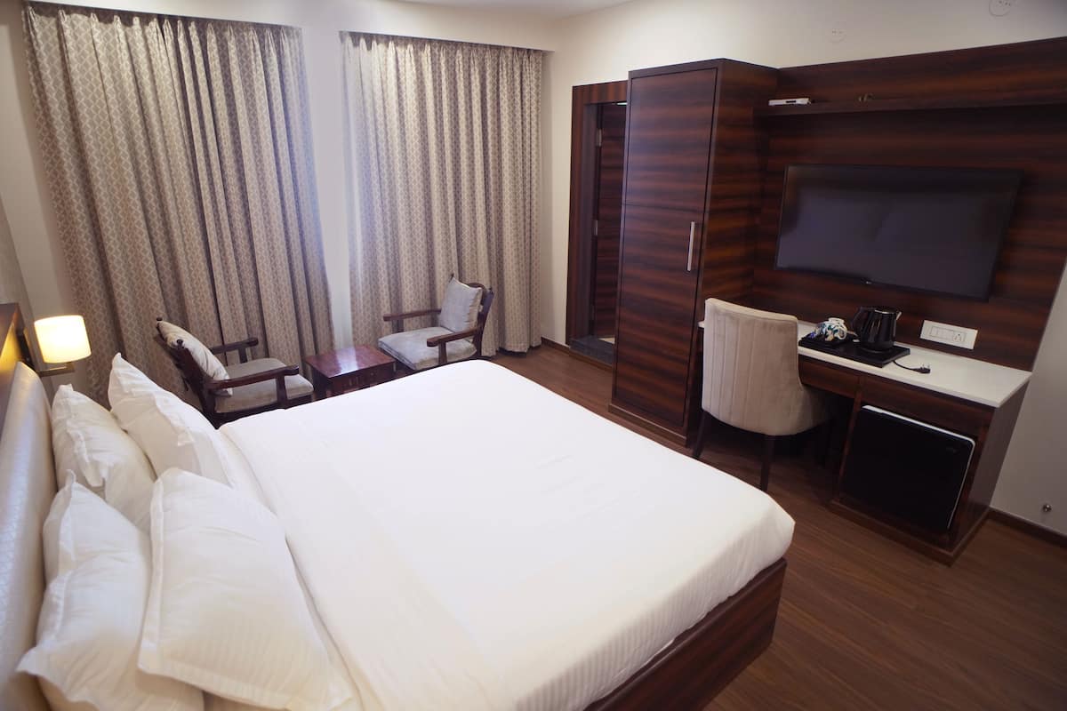 Una habitación de hotel con una cama grande, un escritorio con silla, un televisor y un armario.