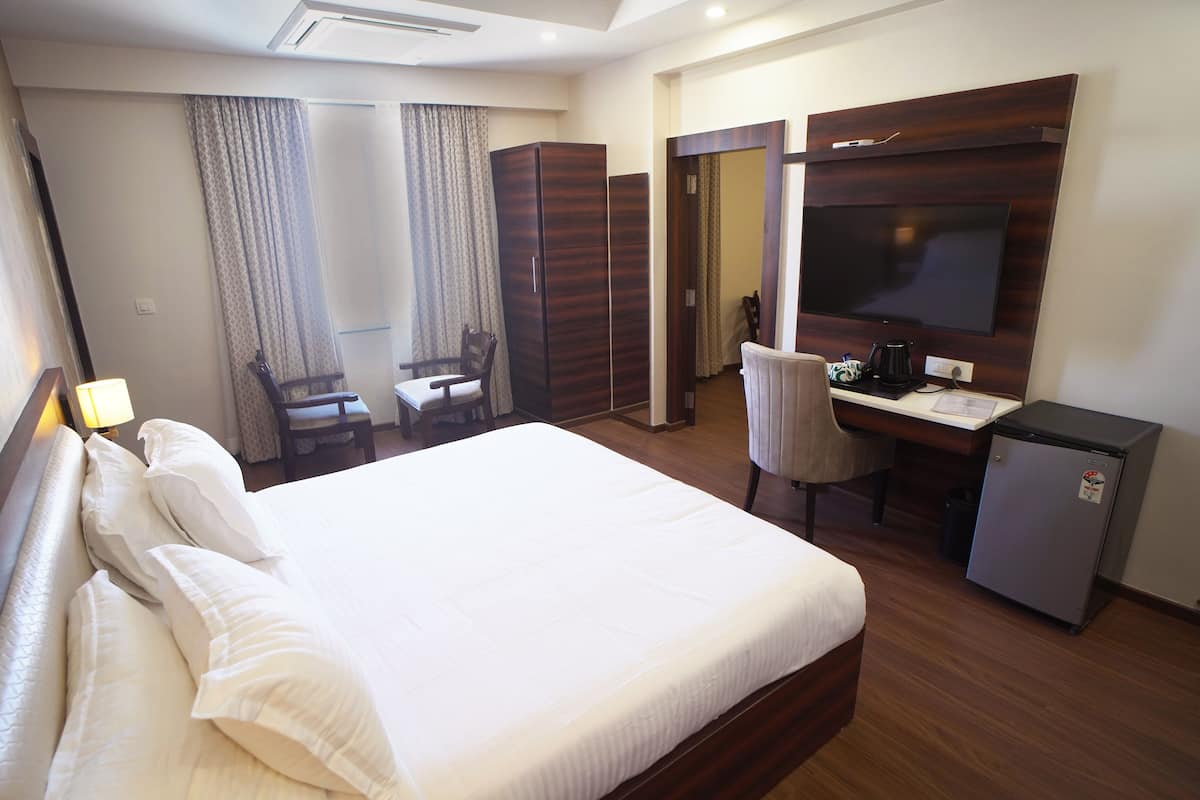 Habitación de hotel con una cama grande, un escritorio con computadora, una silla, un refrigerador pequeño y un televisor montado en la pared.