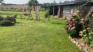 A well-maintained lawn with a wooden play structure, a small garden with pink flowers, and a building with a sloped roof.