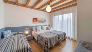A room with two beds, wooden beams on the ceiling, a painting on the wall, and a window with curtains.