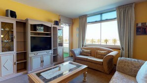 A living room with a sofa, TV, and cabinets. - Palo Alto Holiday Condo Bloubergstrand (Cape Town)