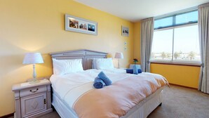 A hotel room with a large bed, two bedside tables with lamps, a nightstand with a drawer, and a window with curtains. - Palo Alto Holiday Condo Bloubergstrand (Cape Town)