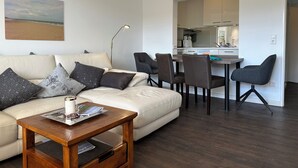 A modern living room with a sofa, coffee table, and dining area. - Robby 6 - Near the beach, quiet apartment with balcony (Wangerooge)