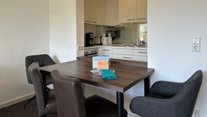 A dining area with a table, chairs, and a kitchen in the background. - Robby 6 - Near the beach, quiet apartment with balcony (Wangerooge)