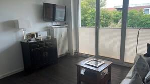 A living room with a flat-screen TV mounted on the wall, a wooden coffee table, a sofa, and a radiator. - Robby 6 - Near the beach, quiet apartment with balcony (Wangerooge)