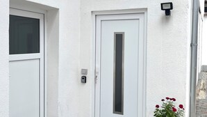 Eine weiße Tür mit kleinem Fenster, einer kleinen Außenleuchte und einem roten Blumenkasten.