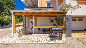 Eine Terrassengruppe mit Grill, Steinbelag und einer Holz-Pergola.