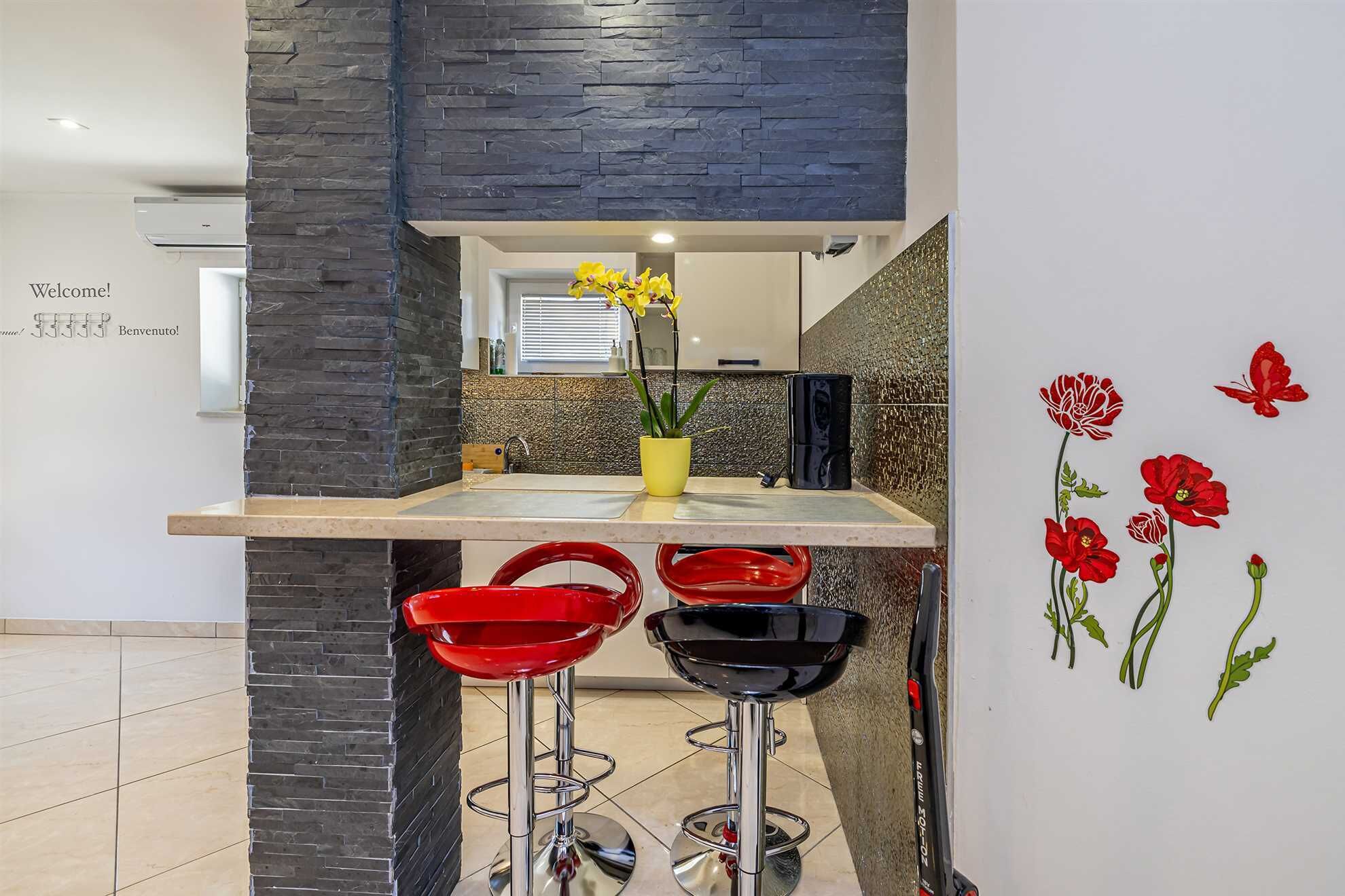 A modern kitchen with a stone accent wall, a bar area with red stools, and a decorative wall with red flowers.