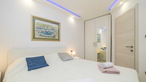 Ein Schlafzimmer mit Bett, Kissen, Nachttisch, Lampe, einem gerahmten Bild, einem Kleiderschrank und einem Spiegel.
