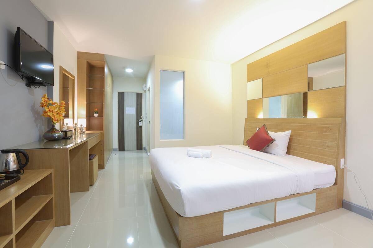 Una habitación de hotel moderna con una cama grande, un escritorio con televisor de pantalla plana, una mesita de noche de madera y un armario empotrado.